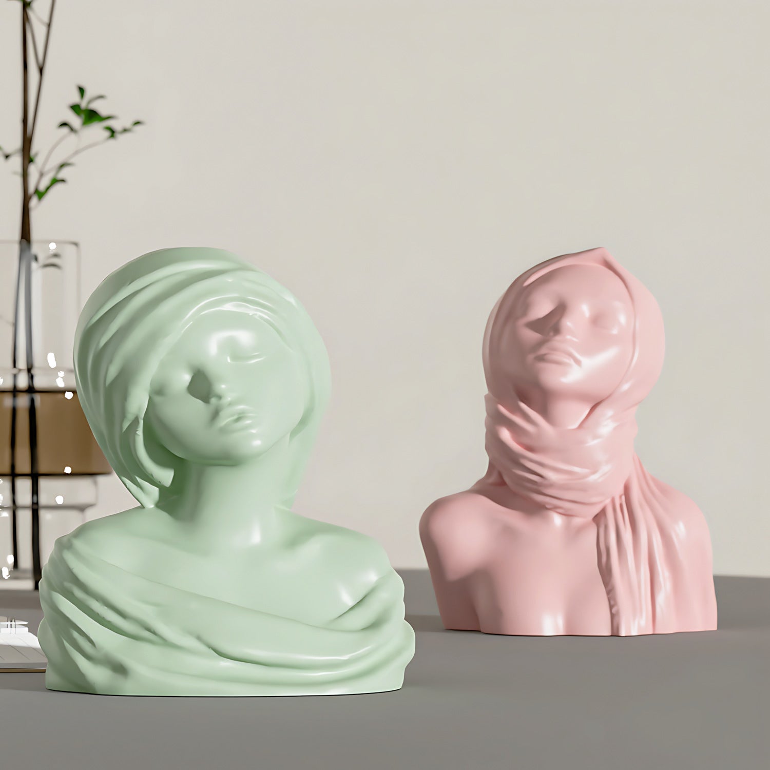 Two ceramic busts, one green and one pink, with veils on a neutral background.